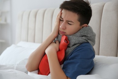 Sick teenage boy with hot water bottle in bed at home