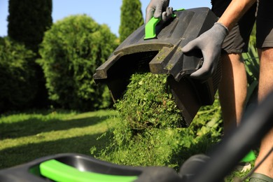 Photo of Man removing grass out of lawn mower box in garden, closeup