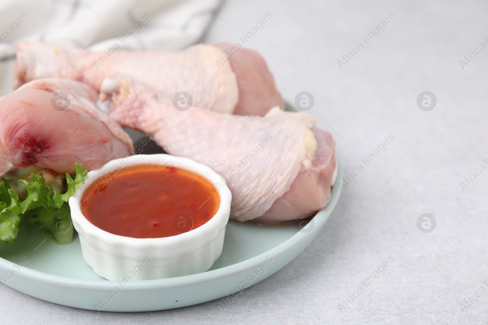 Photo of Fresh marinade, raw chicken drumsticks and lettuce on light table, closeup. Space for text
