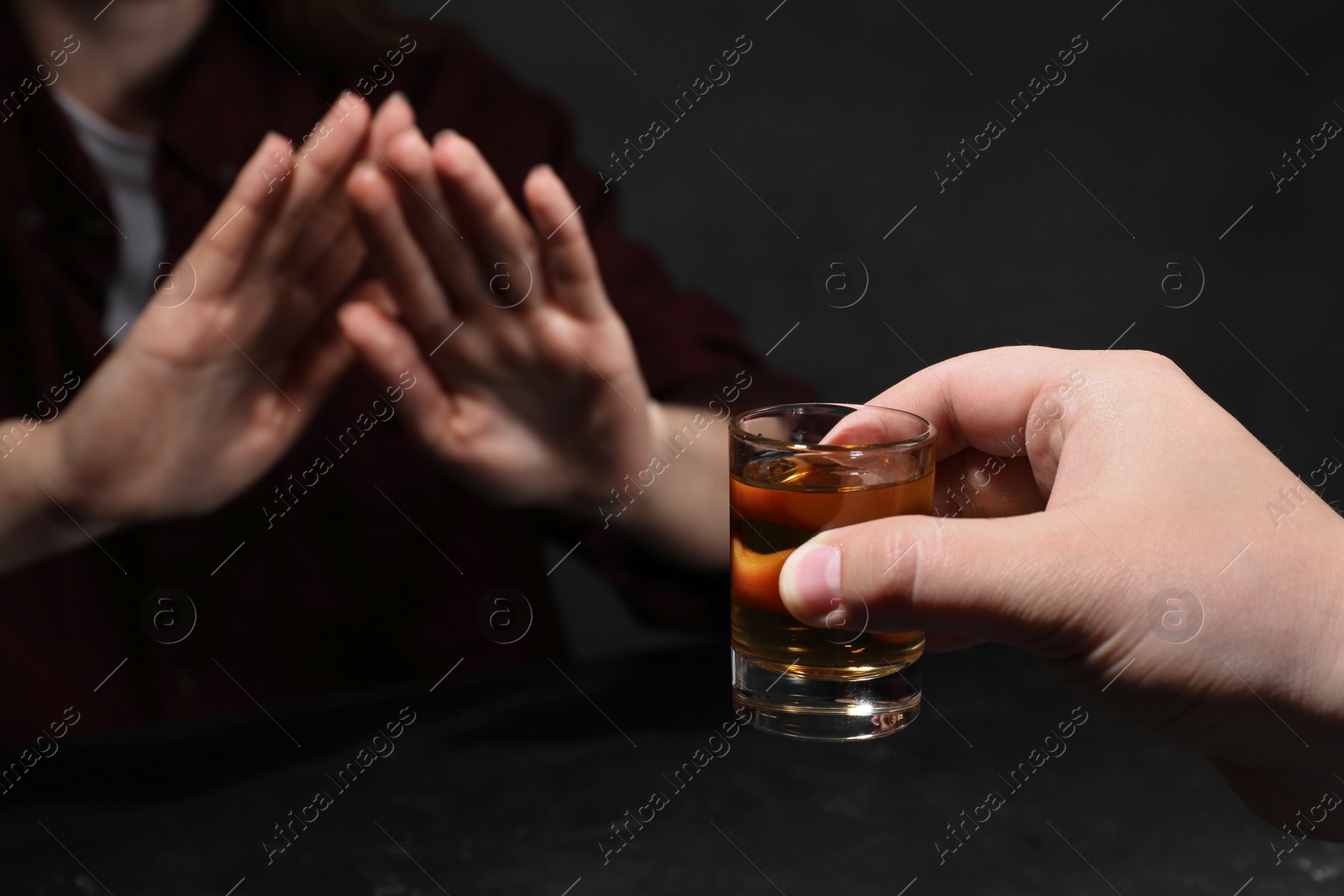 Photo of Alcohol addiction. Woman refusing glass of whiskey at dark table, selective focus