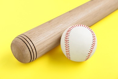 Photo of Wooden baseball bat and ball on yellow background, closeup. Sports equipment