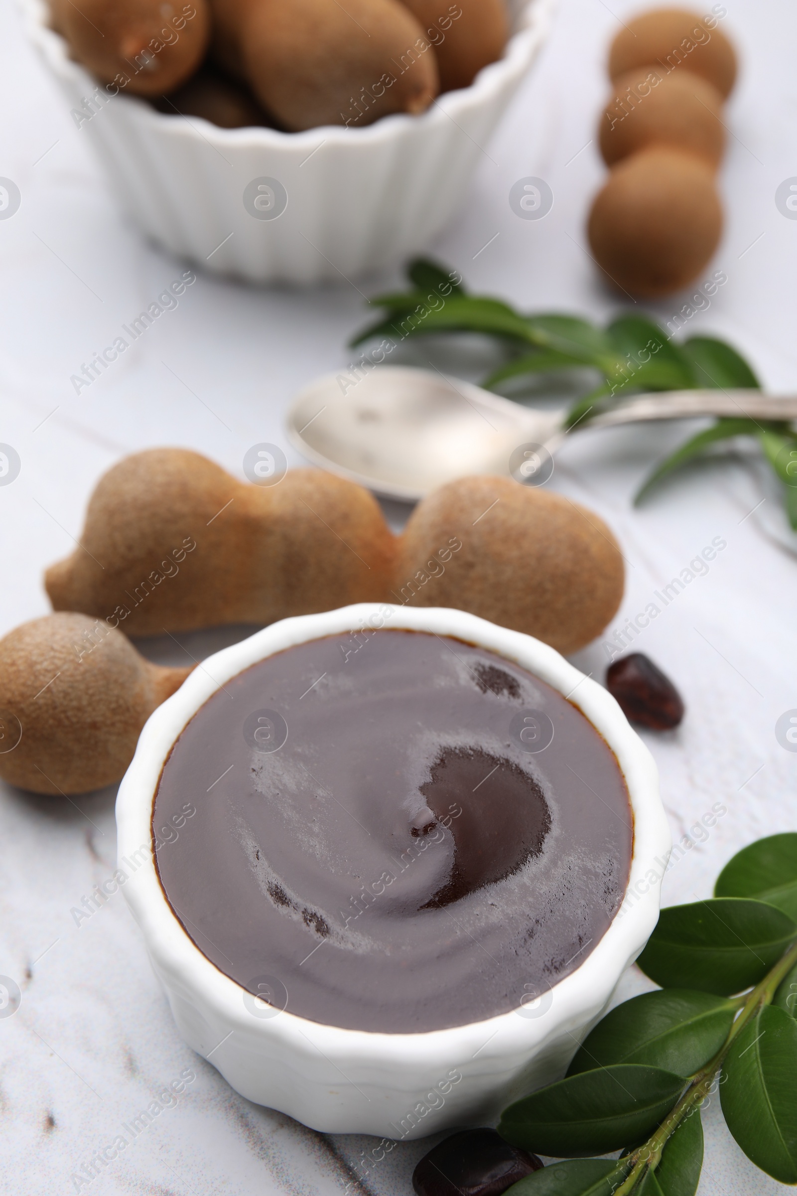 Bowl of tasty tamarind sauce and fresh pods on white textured table Photo of Bowl of tasty tamarind sauce and fresh pods on white textured table