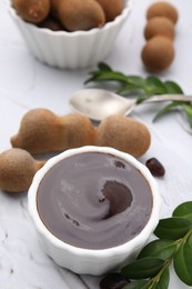 Photo of Bowl of tasty tamarind sauce and fresh pods on white textured table