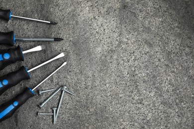 Photo of Set of screwdrivers and screws on grey table, top view. Space for text