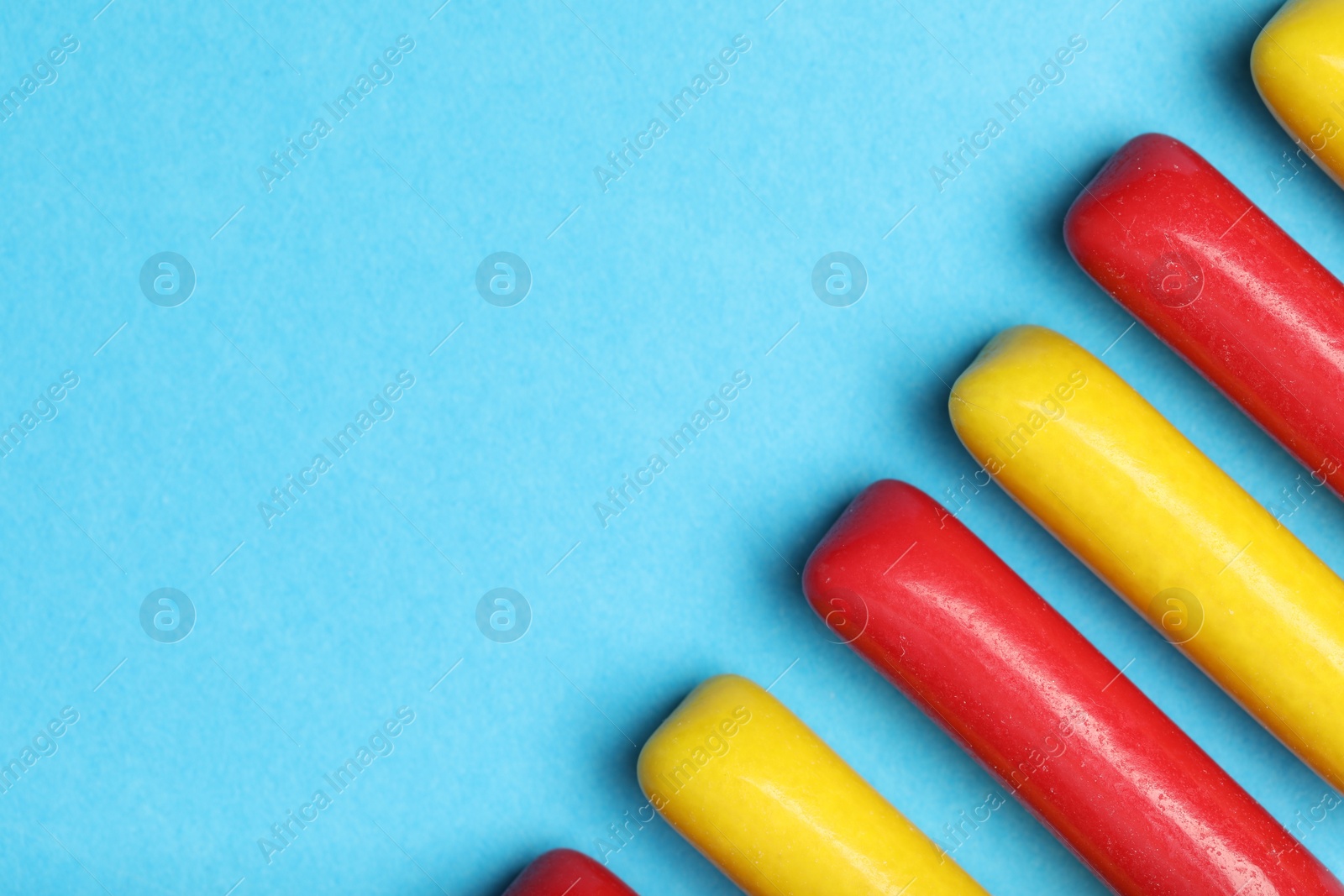 Photo of Many tasty bubble gums on light blue background, flat lay. Space for text