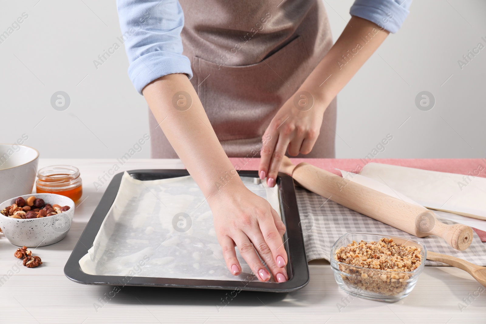 Photo of Woman making delicious baklava at white wooden table, closeup