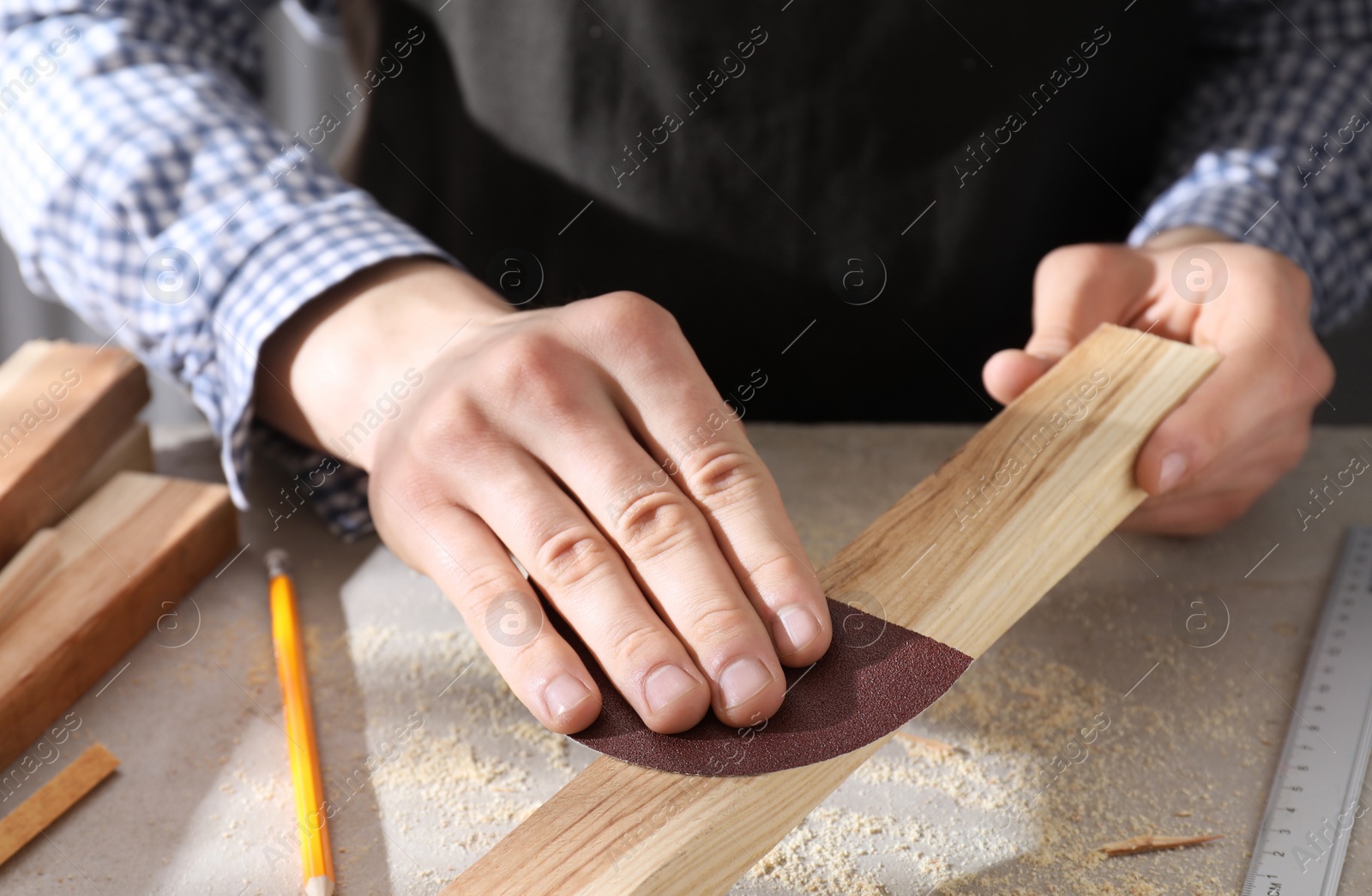 Photo of Man polishing wooden plank with sandpaper at grey table, closeup