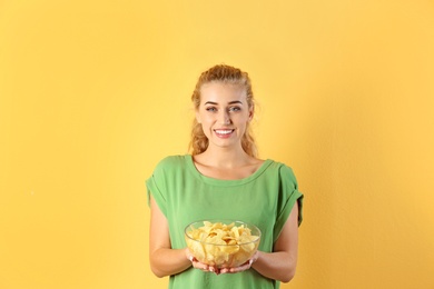 Woman with bowl of potato chips on color background