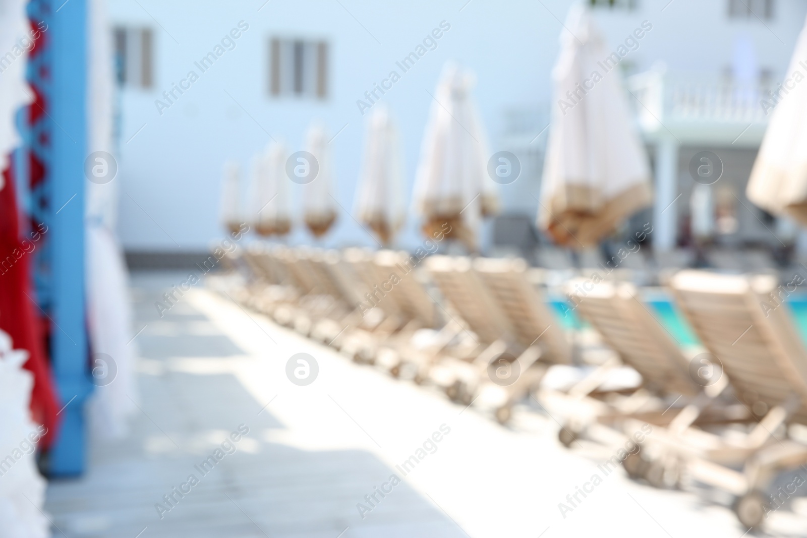 Photo of Blurred view of comfortable sunbeds near outdoor swimming pool at resort on sunny day