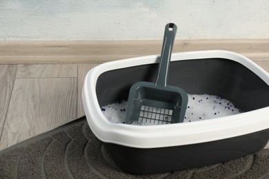 Cat tray with crystal litter and scoop on floor indoors