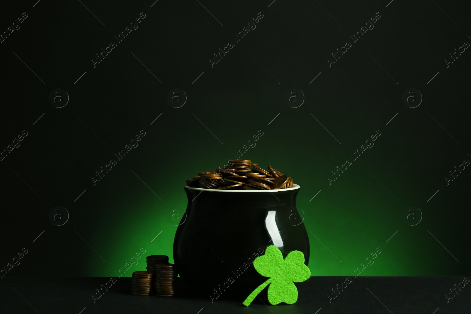 Photo of Pot with gold coins and clover on table against dark background. St. Patrick's Day