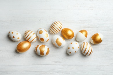 Photo of Flat lay composition of traditional Easter eggs decorated with golden paint on wooden background, top view