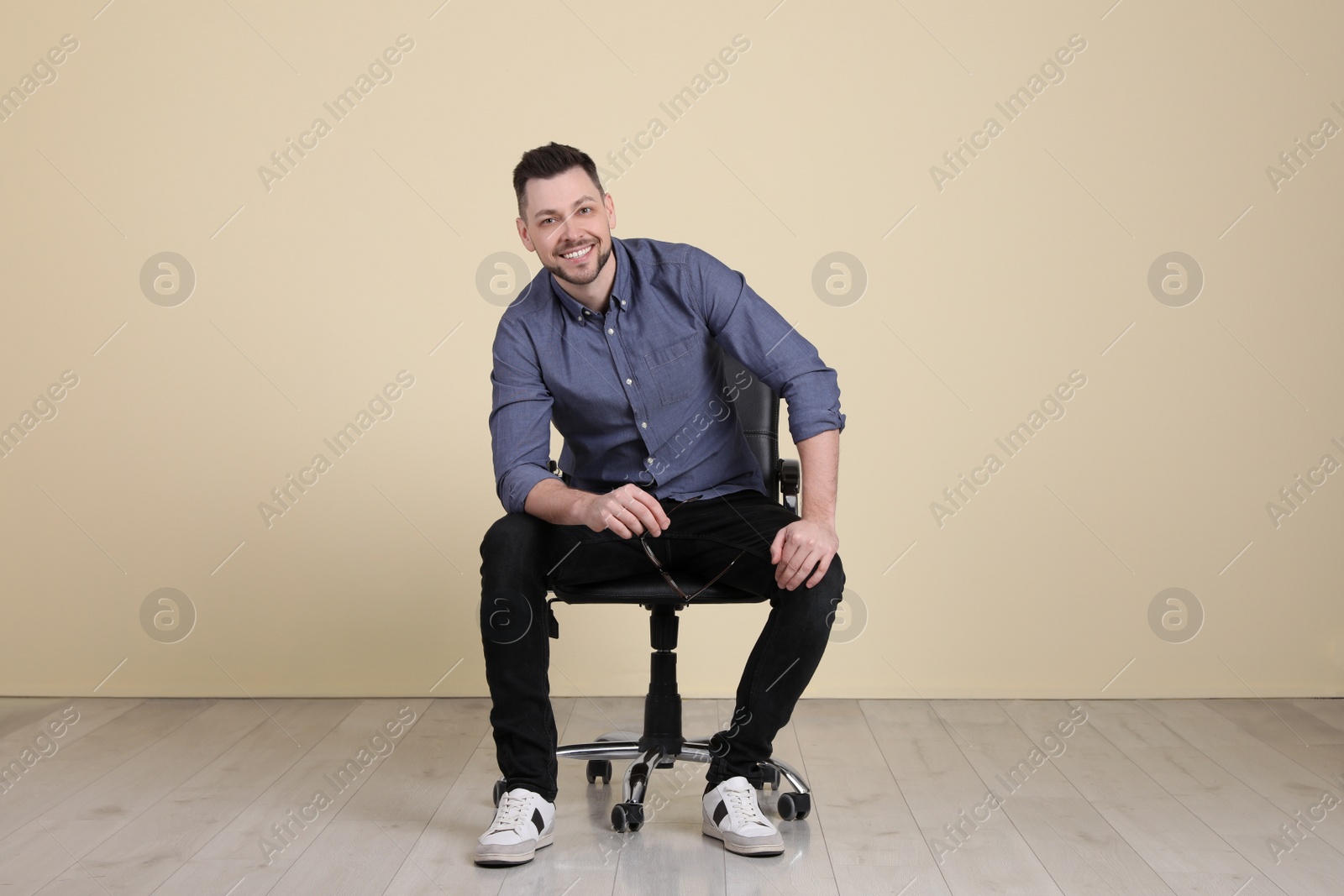 Photo of Handsome man with glasses sitting in office chair near beige wall indoors