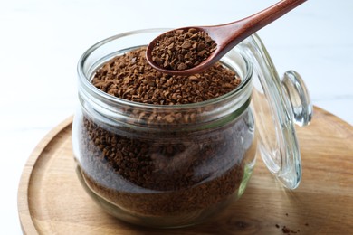 Spoon of instant coffee over jar on white table, closeup