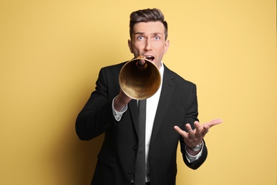 Young man using megaphone on color background