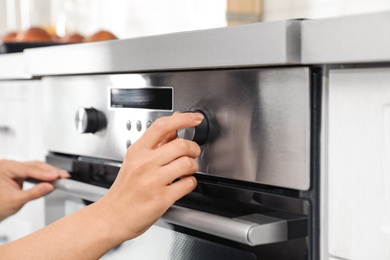 Photo of Woman regulating cooking mode on oven panel in kitchen, closeup