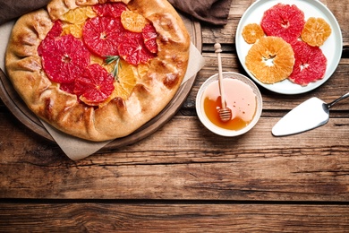 Photo of Tasty galette with citrus fruits and rosemary served on wooden table, flat lay. Space for text