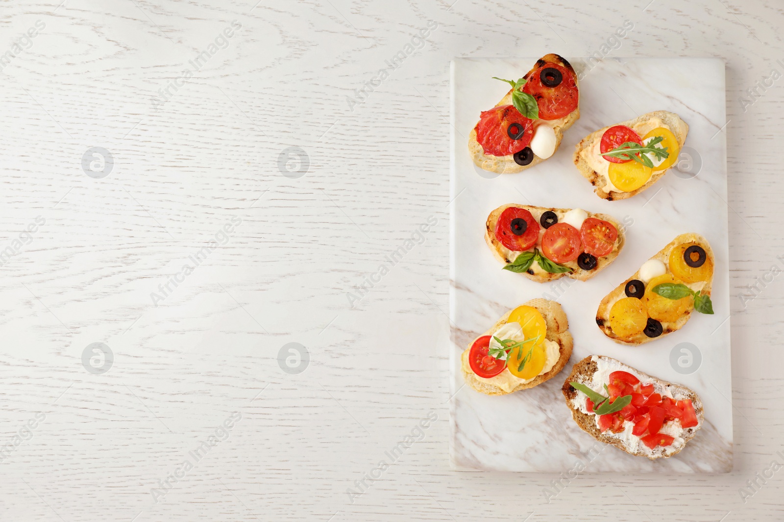 Photo of Marble board with delicious tomato bruschettas on white wooden background, top view. Space for text