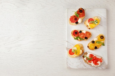 Marble board with delicious tomato bruschettas on white wooden background, top view. Space for text