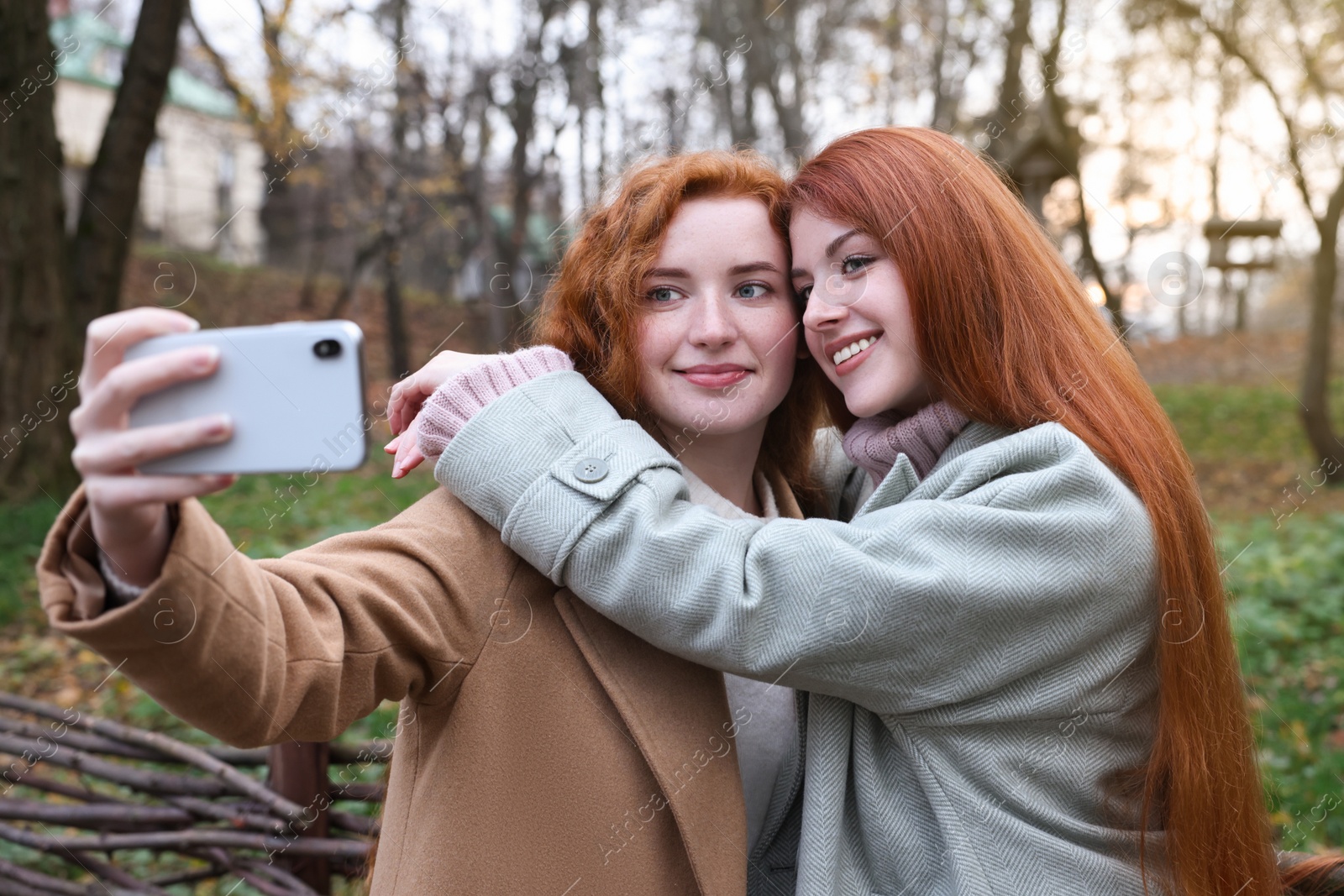 Photo of Beautiful young redhead sisters taking selfie in park on autumn day