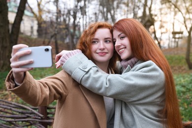 Photo of Beautiful young redhead sisters taking selfie in park on autumn day