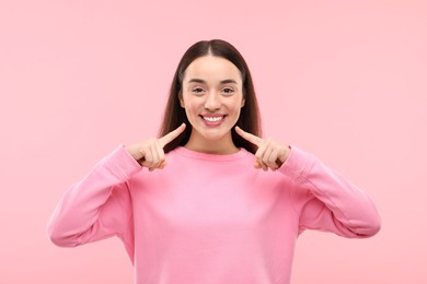 Beautiful woman showing her clean teeth and smiling on pink background