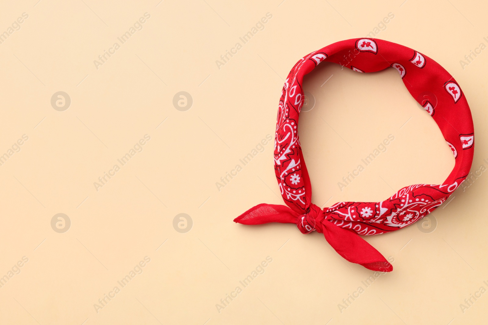 Photo of Tied red bandana with paisley pattern on beige background, top view. Space for text