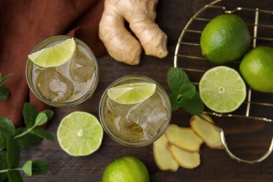 Photo of Glasses of tasty ginger ale with ice cubes and ingredients on wooden table, flat lay