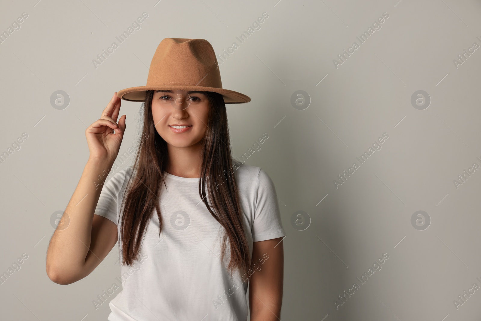Photo of Smiling young woman in stylish outfit on light grey background. Space for text