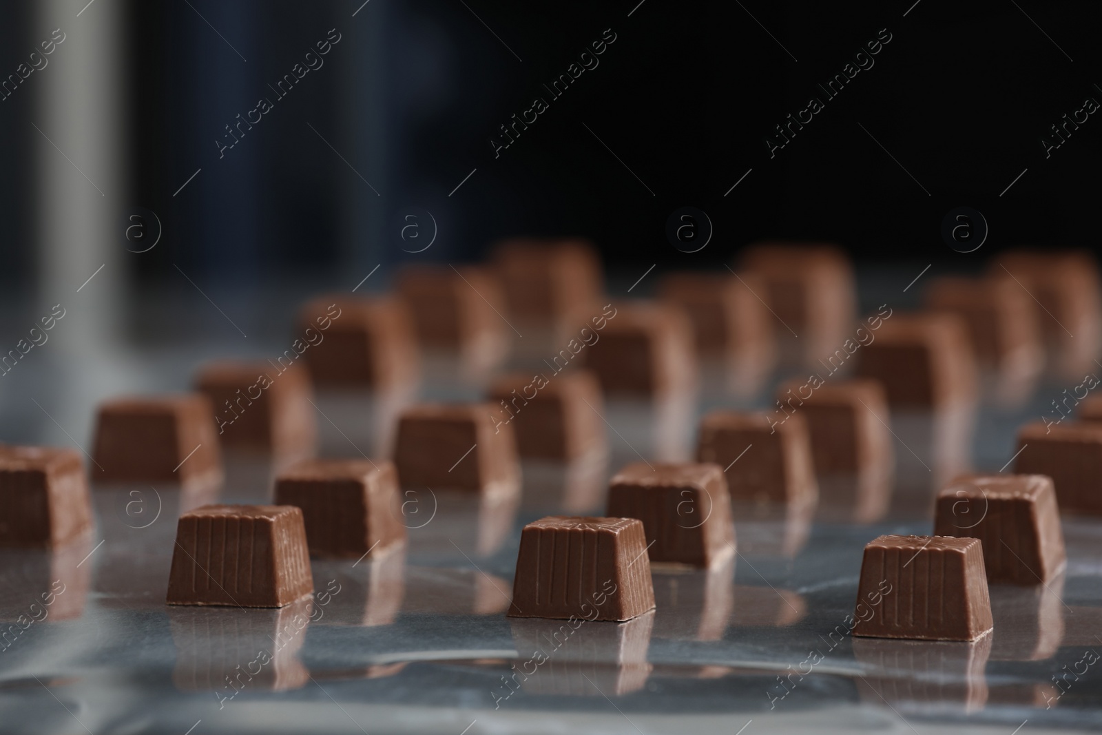 Photo of Many delicious chocolate candies on production line, closeup