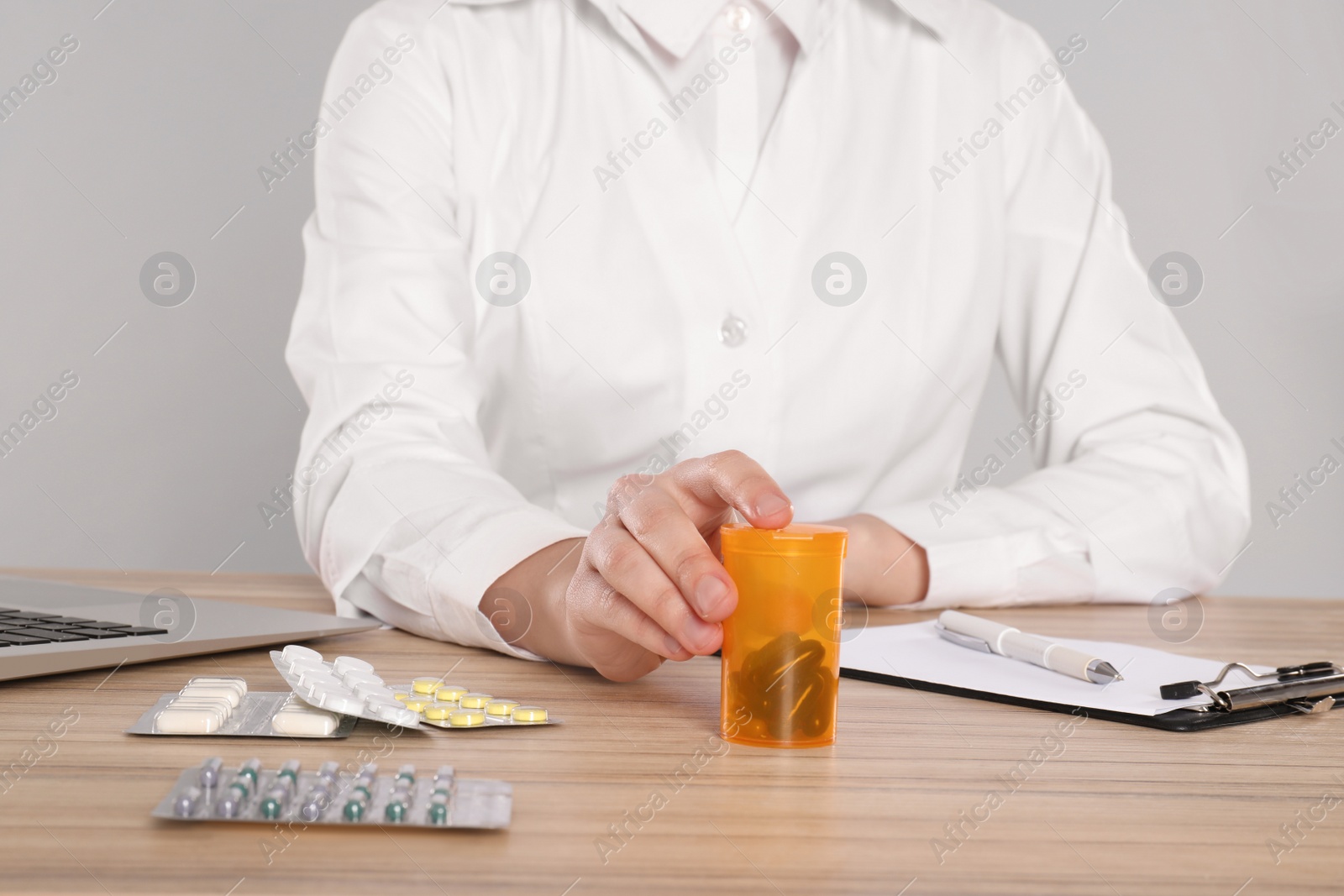 Photo of Professional pharmacist working at table against light grey background, closeup