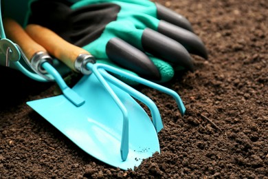 Photo of Overturned bucket with gardening tools and gloves on fresh soil, closeup