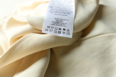 Photo of Clothing label with care instructions on beige garment, closeup