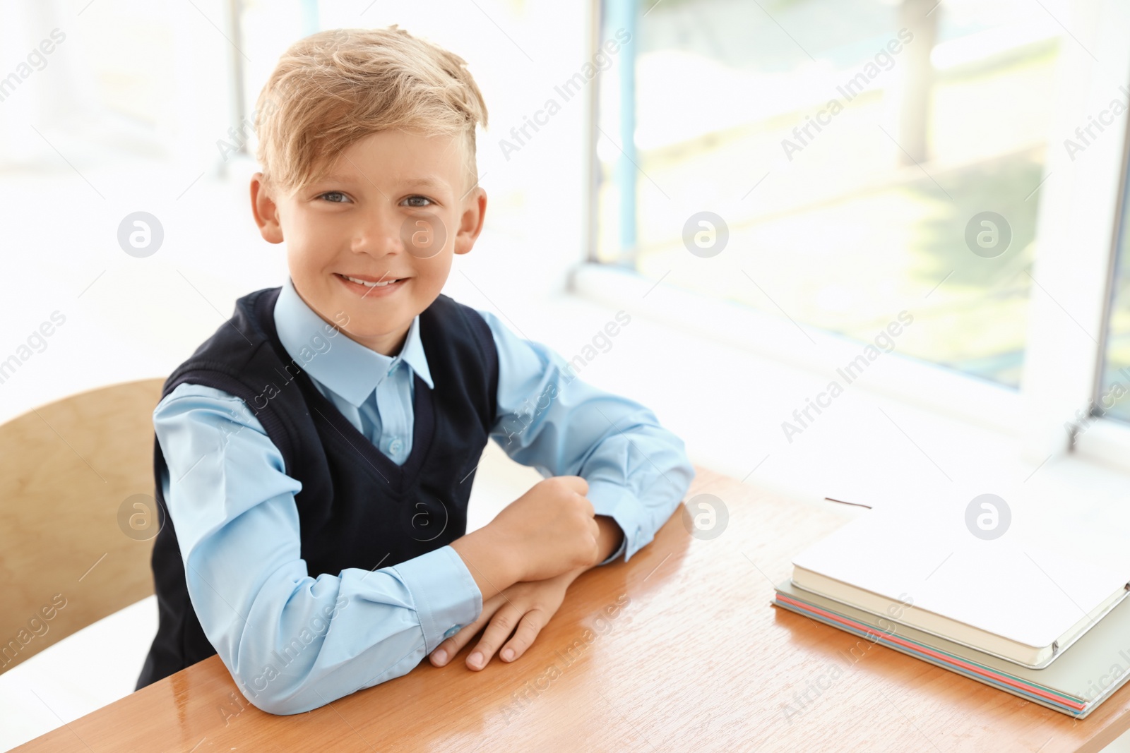 Photo of Little boy in stylish school uniform at desk