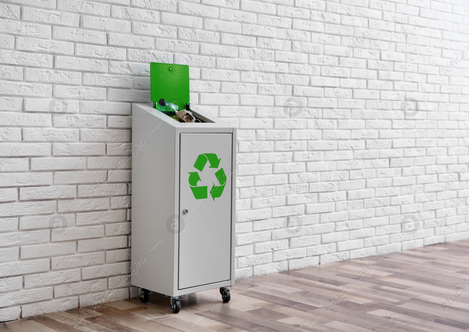 Photo of Overfilled trash bin with recycling symbol near brick wall indoors. Space for text