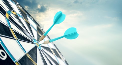 Image of Dart board with light blue arrows hitting target against sky, space for text. Banner design