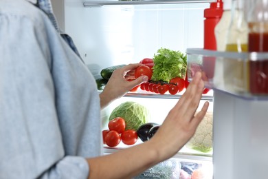 Photo of Young woman taking tomato out of refrigerator, closeup