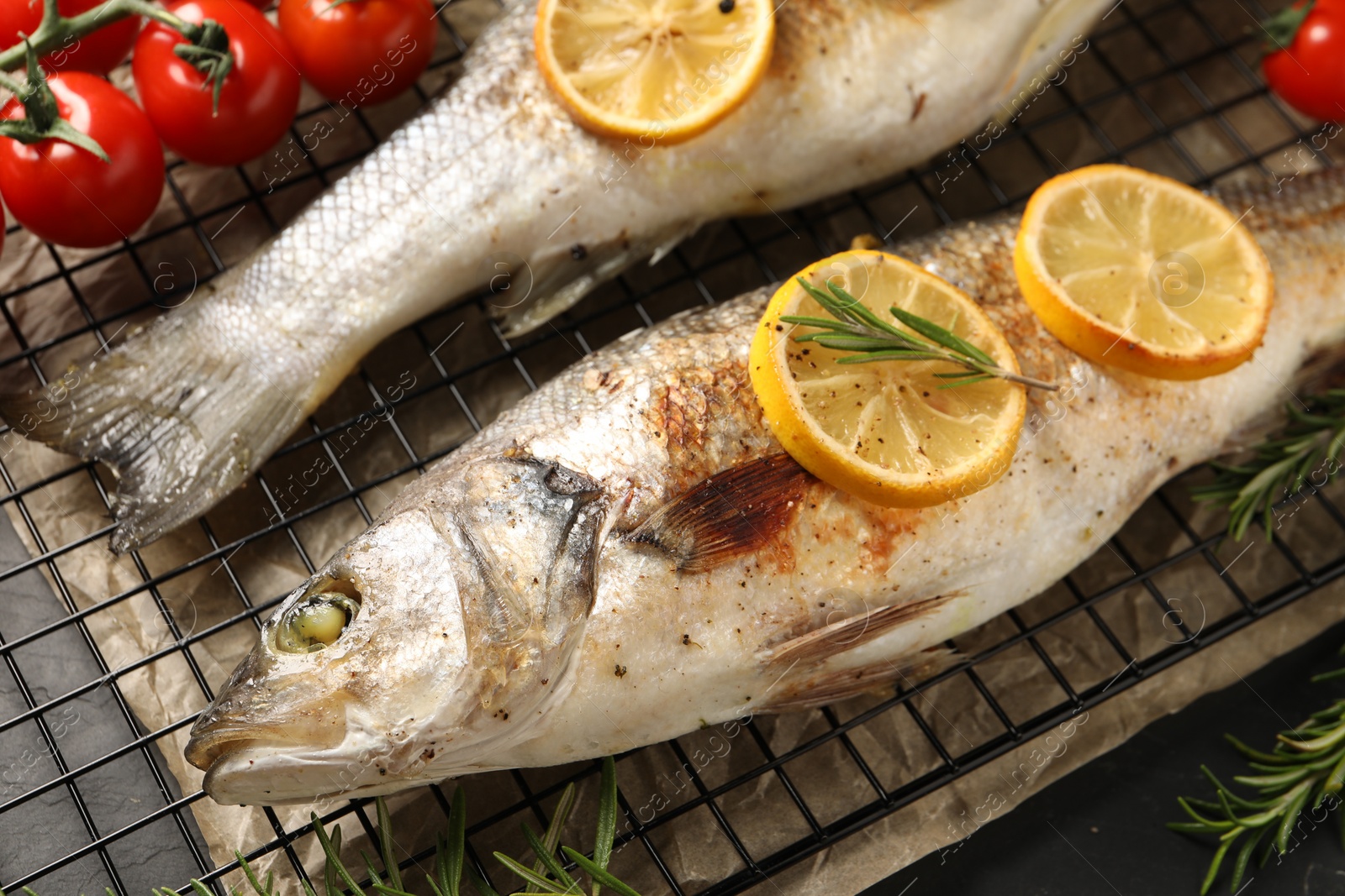 Photo of Baked fish with tomatoes, rosemary and lemon on black table, closeup