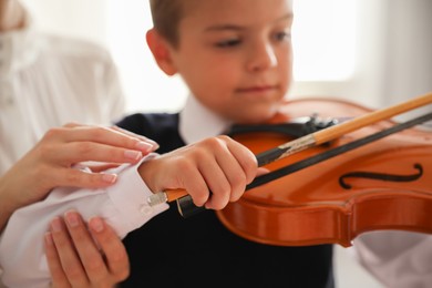 Young woman teaching little boy to play violin indoors, focus on hands
