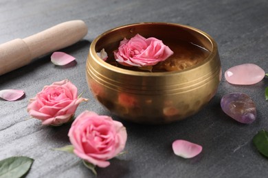 Photo of Tibetan singing bowl with water, beautiful rose flowers, mallet and stones on gray table, closeup