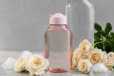 Photo of Micellar water and roses on grey table, closeup