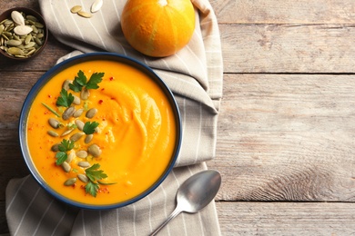 Flat lay composition with pumpkin cream soup in bowl on wooden background. Space for text