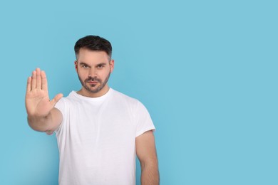 Handsome man showing stop gesture on light blue background, space for text