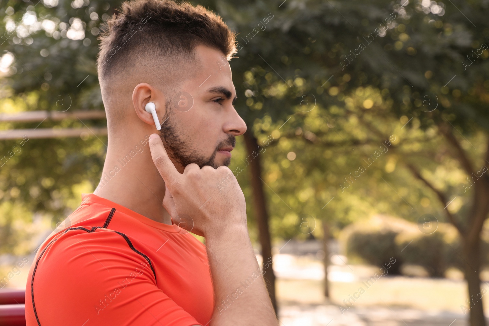 Photo of Young man with wireless headphones listening to music on sports ground. Space for text