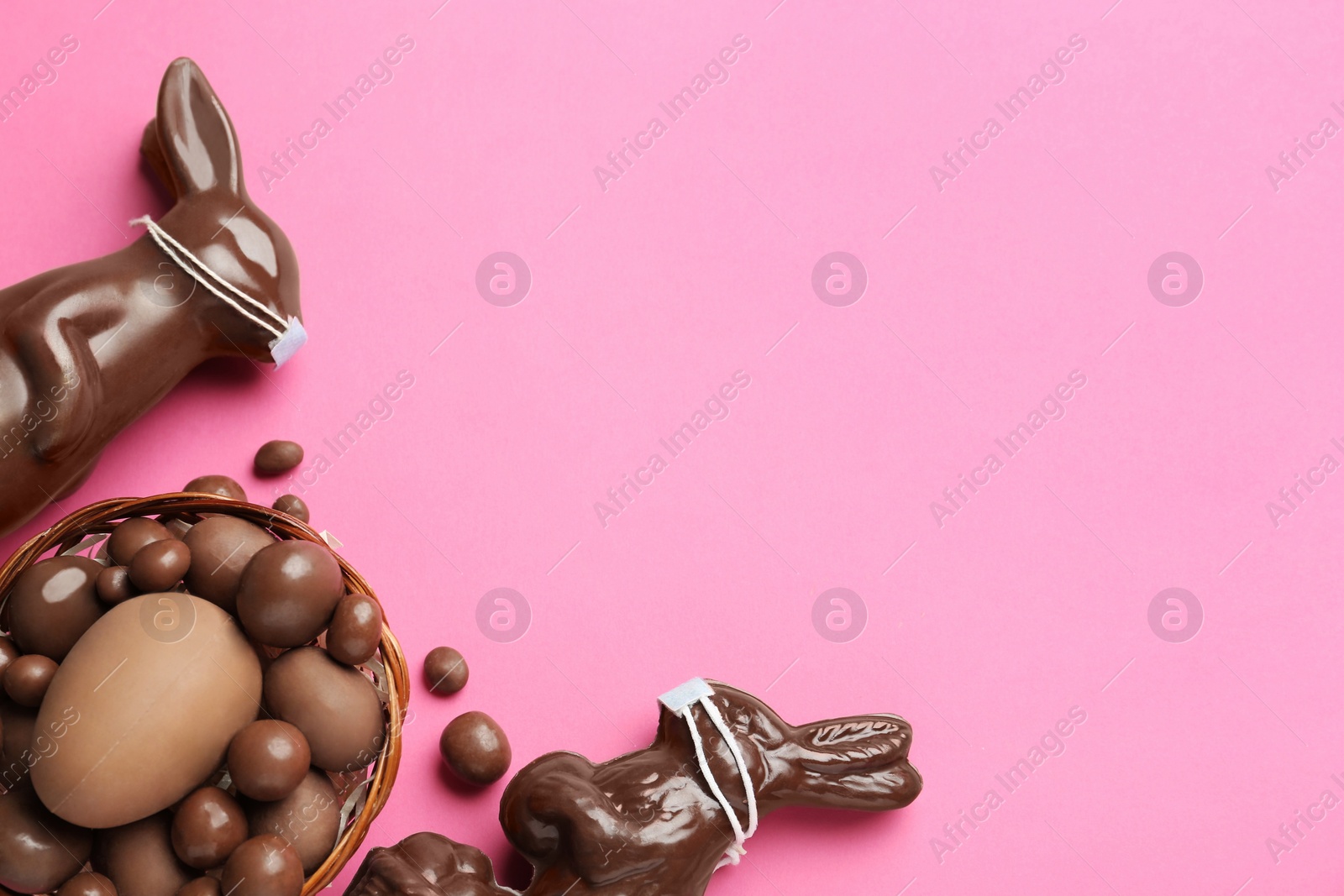 Photo of Chocolate bunnies with protective masks, candies and space for text on pink background, flat lay. Easter holiday during COVID-19 quarantine