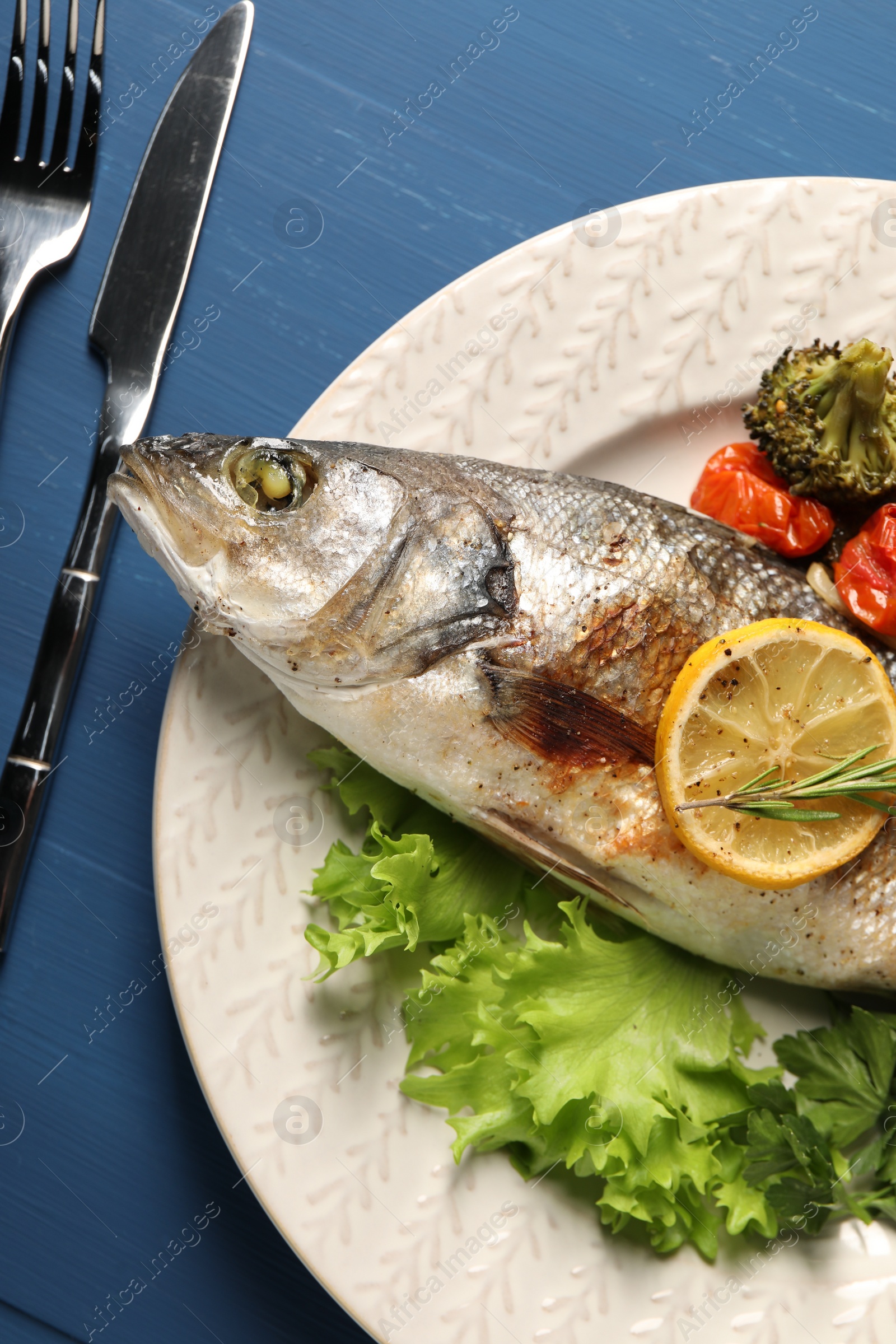 Photo of Delicious baked fish and vegetables served on blue wooden table, top view