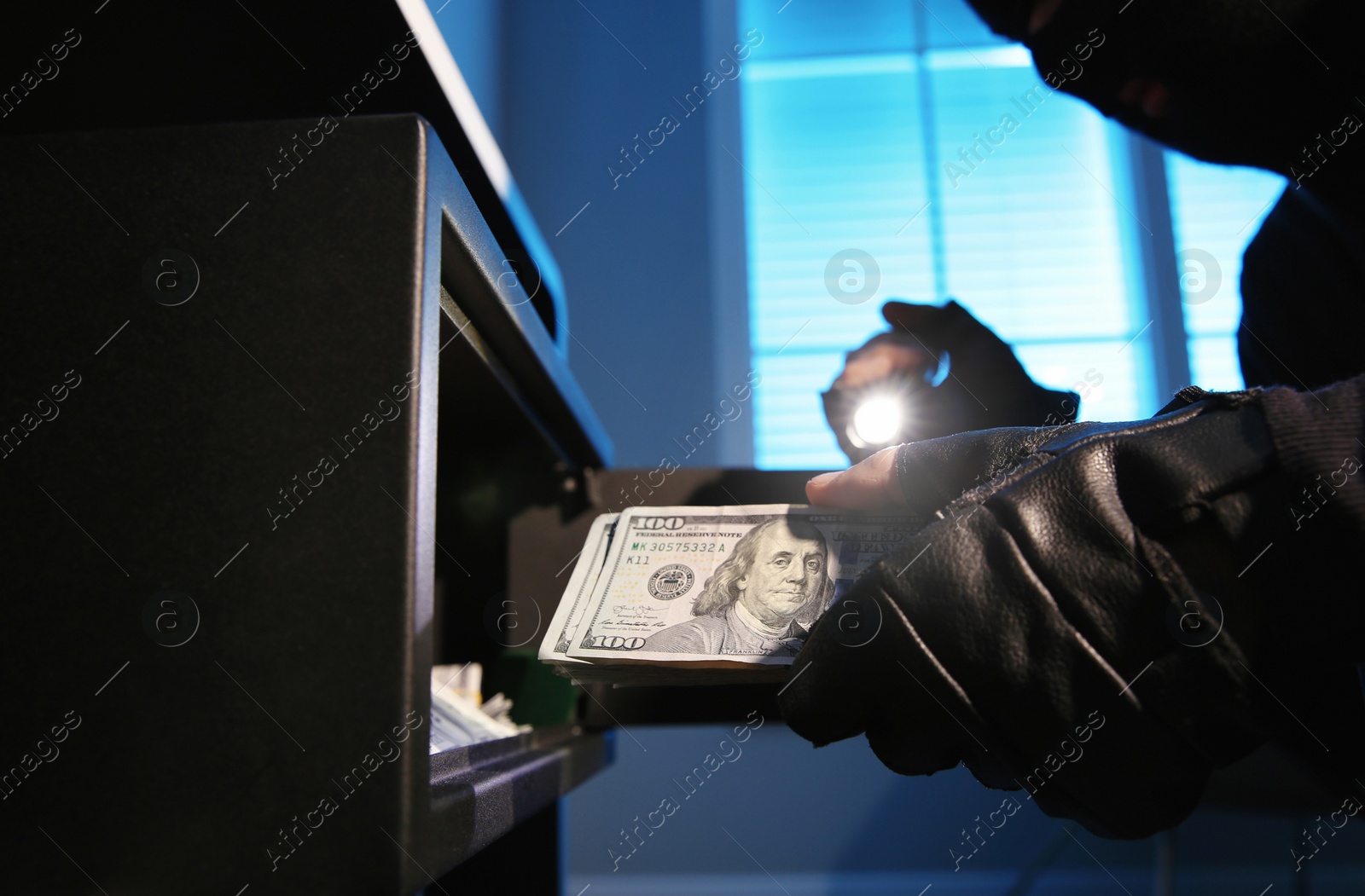 Photo of Thief taking money out of steel safe indoors at night, closeup