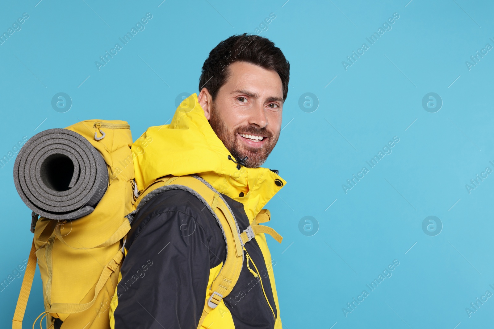 Photo of Happy man with backpack on light blue background, space for text. Active tourism