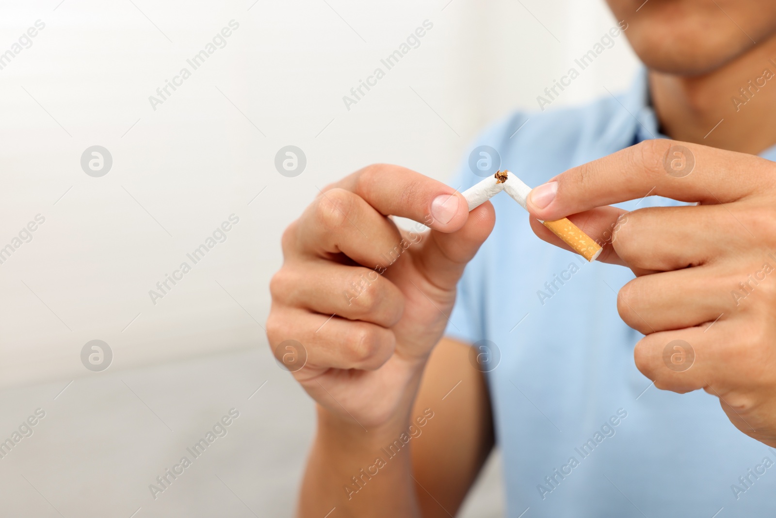 Photo of Stop smoking concept. Young man breaking cigarette on blurred background, closeup. Space for text