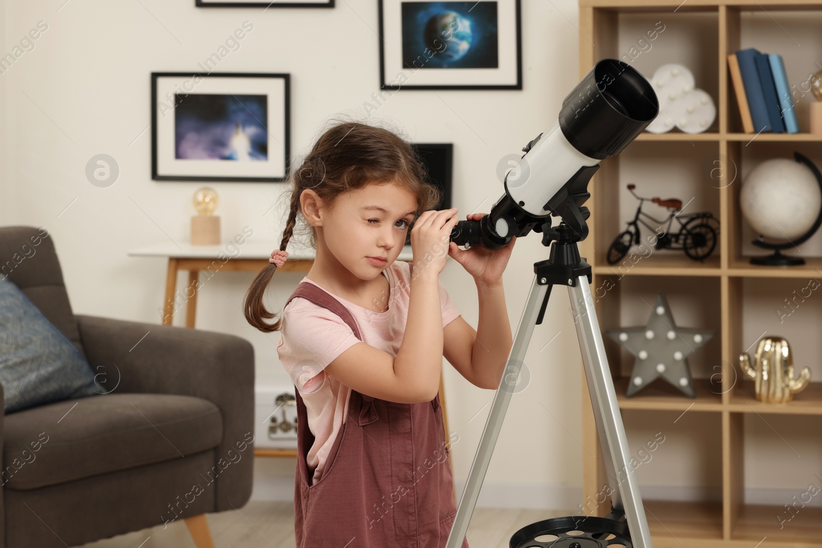 Photo of Cute little girl looking at stars through telescope in room